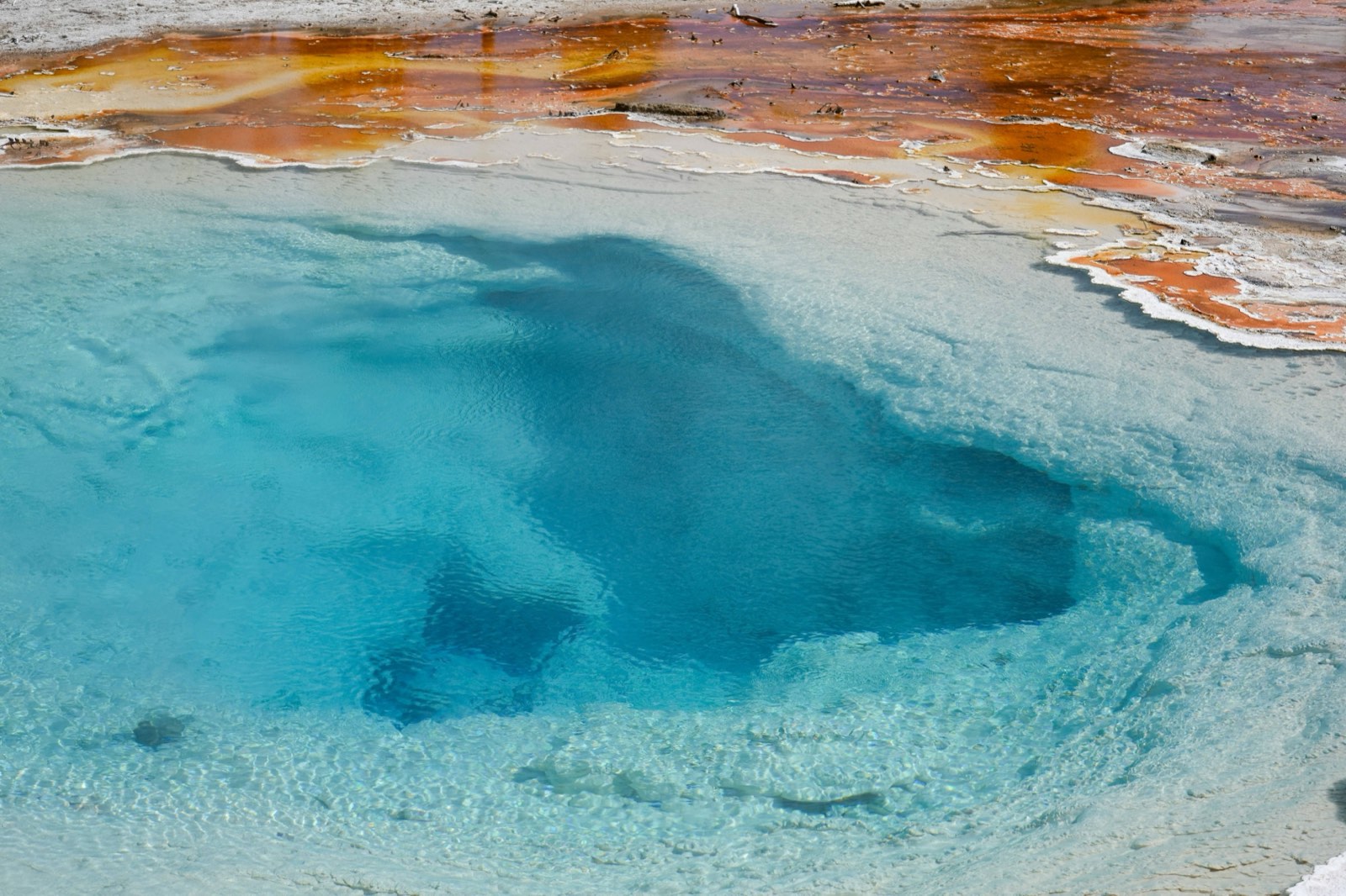 Vivid blue geothermal hot spring with mineral-stained banks